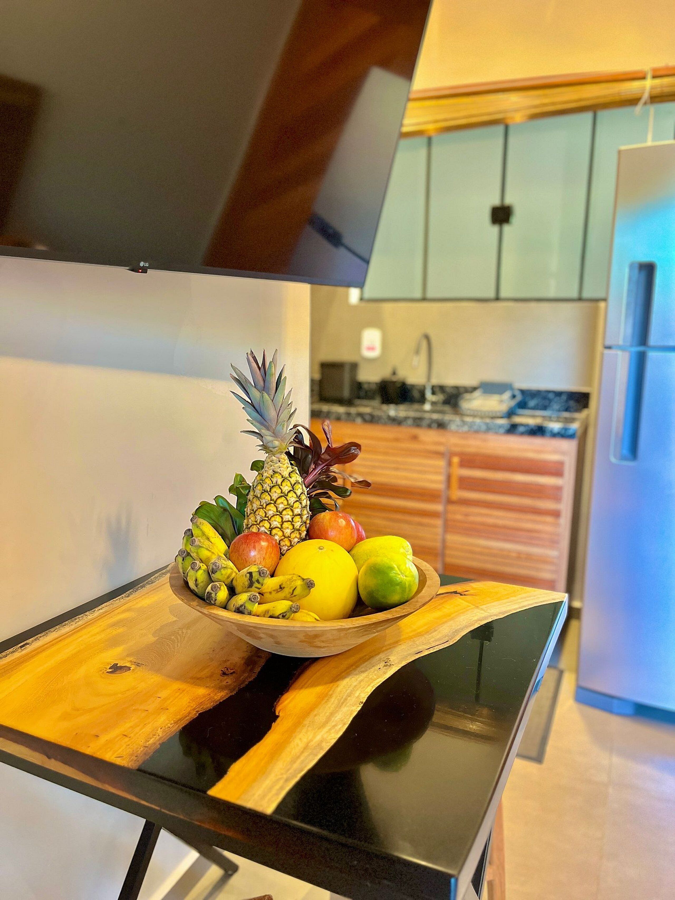 Een keuken met een houten schaal fruit op een glazen tafel.