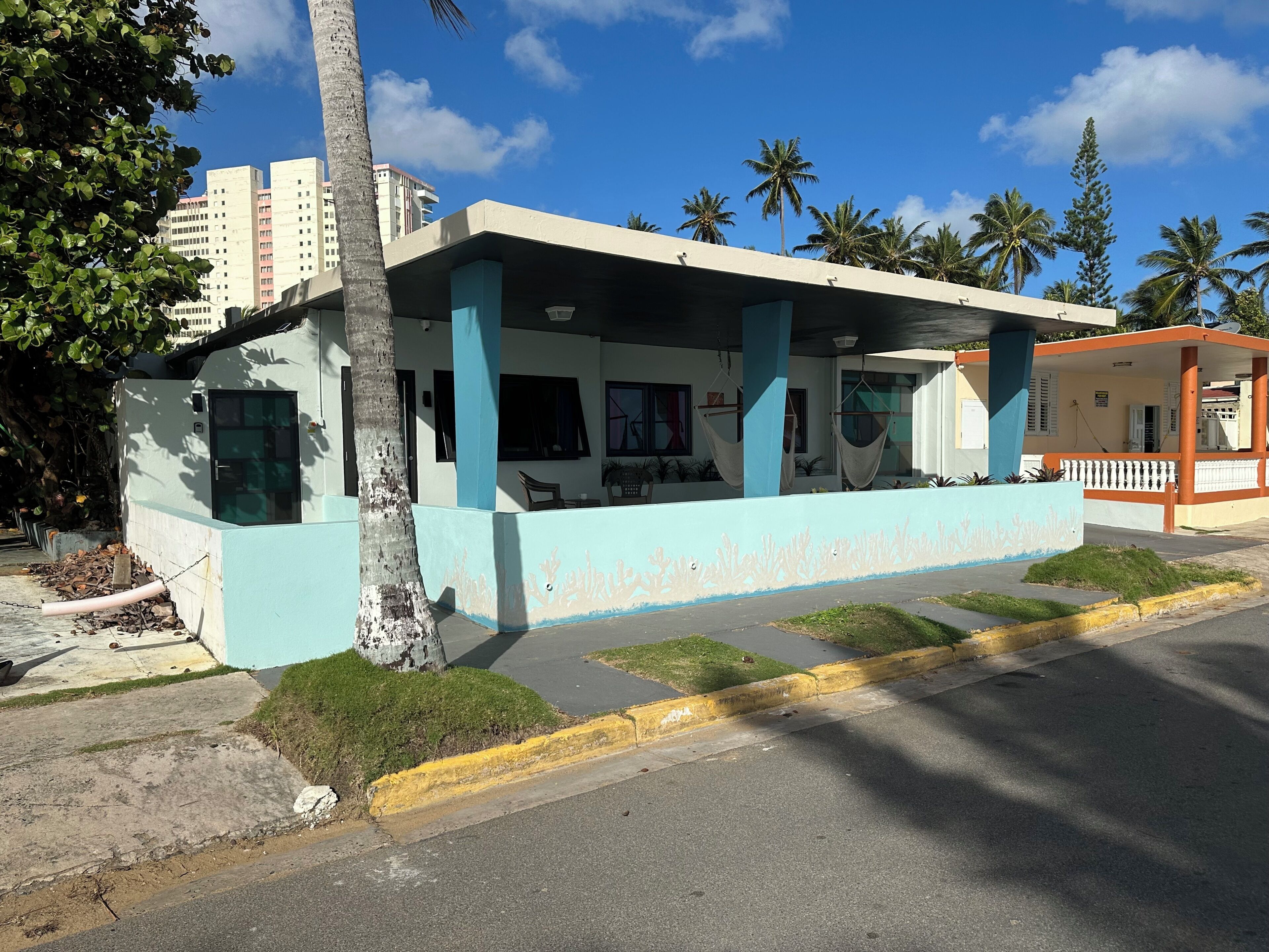 Un edificio con fachada azul claro, un porche cubierto y una pequeña estructura adyacente con barandal blanco.