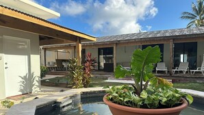 Un espace piscine agrémenté d’un pot de fleurs au centre, entouré de chaises longues et d’une terrasse couverte.