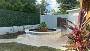 Un jardin aménagé avec un élément aquatique central, entouré d’un petit muret et agrémenté de différentes plantes.