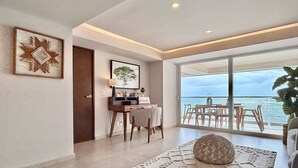 Una sala de estar moderna con un gran ventanal con vistas al mar, un comedor con mesa y sillas, y una zona de estar acogedora con alfombra y un cojín decorativo.