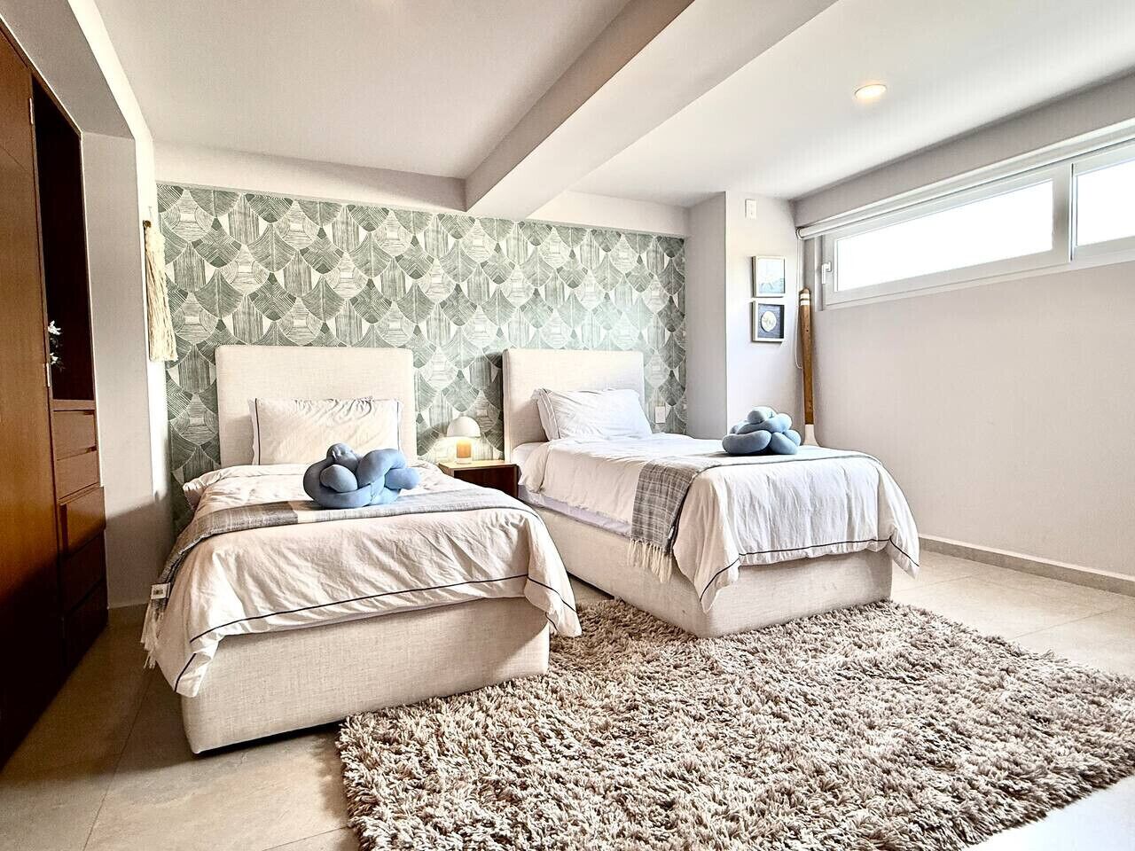 A bedroom with two beds, a large rug, and a geometric patterned wall.