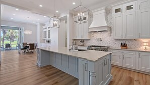 Una cocina amplia con una isla grande, muebles blancos e iluminación colgante.