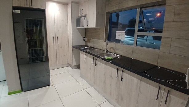 A modern kitchen with light wood cabinets, a black countertop, and a window overlooking a street.