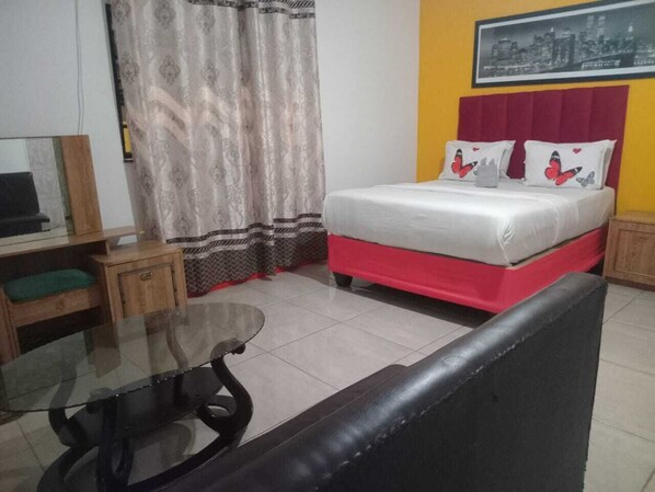 A hotel room with a bed, a small table, a sofa, and a television.