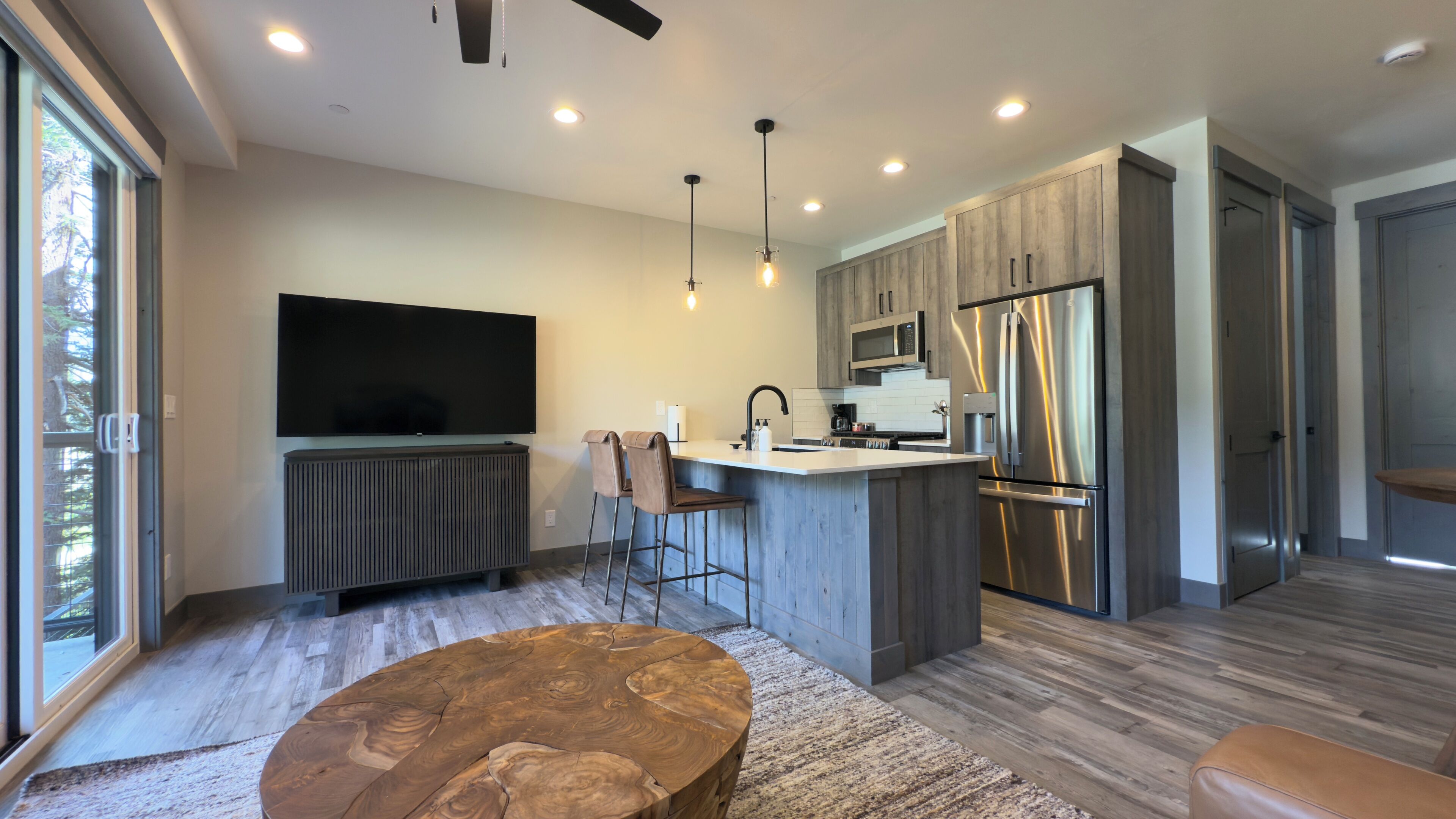A modern kitchen with a large island, stainless steel appliances, and a flat-screen TV mounted on the wall.