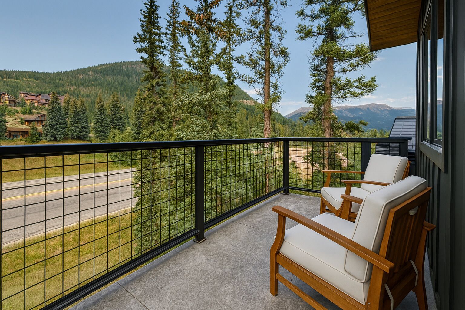 A balcony with a view of a road and forest, wooden chairs, and a metal railing.