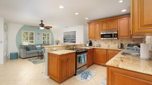 A kitchen with wooden cabinets, a stove, and a microwave. There is a dining area with a table and chairs. - Sunshine Paradise Minutes From Action. Grill, Bikes, Beach Gear & More Included! (Cape Coral)
