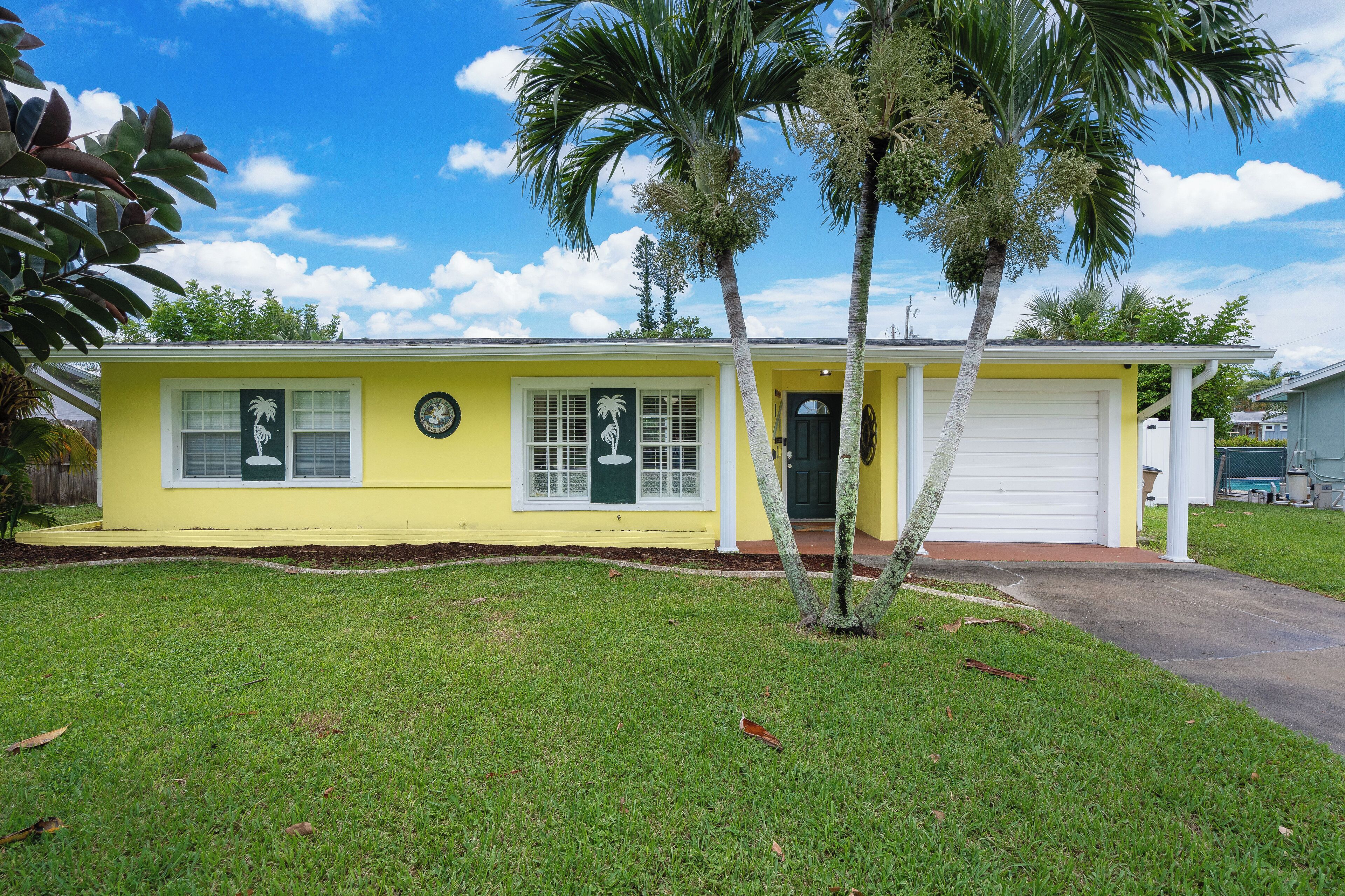 A yellow single-story house with a front porch, palm trees, and a garage.