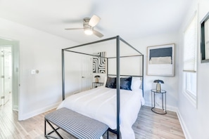 Une chambre à coucher moderne avec un lit à baldaquin, un ventilateur de plafond, une table de chevet avec une lampe et un banc.