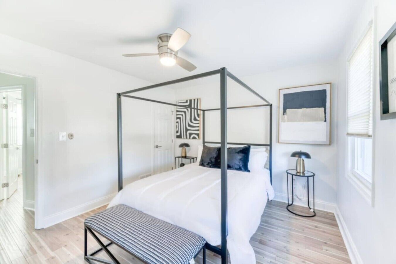 A modern bedroom with a four-poster bed, a ceiling fan, and a bedside table with a lamp.