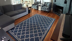 Una sala de estar con sofá, mesa de centro, alfombra estampada, chimenea y mueble para televisión.