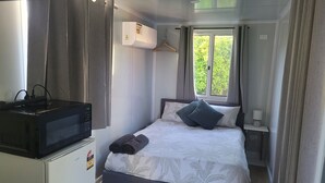 Una habitación compacta con cama, una mesita, microondas y ventana con cortinas.