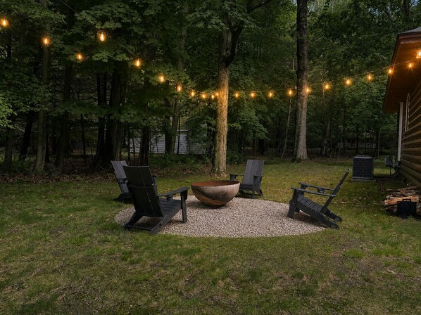 Uma área externa com assentos Adirondack, lareira e luzes de corda.