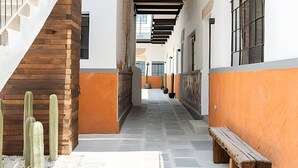 A narrow corridor with a wooden staircase on the left, a bench on the right, and a row of windows along the walls.