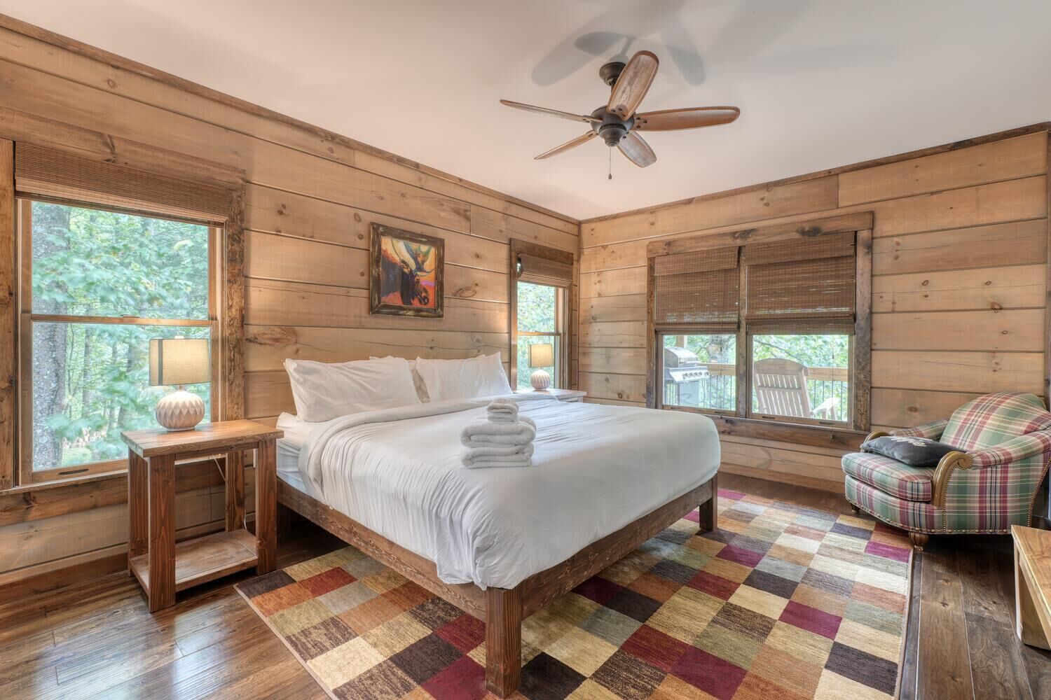 A wooden cabin bedroom with a bed, a chair, a lamp, and a ceiling fan.