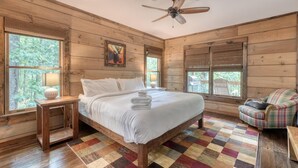 A wooden cabin bedroom with a bed, a chair, a lamp, and a ceiling fan. - Kenny's Place, Suches (Suches)
