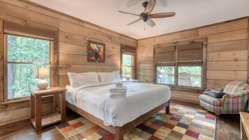 A wooden cabin bedroom with a bed, a chair, a lamp, and a ceiling fan.