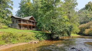 A rustic lodge with a balcony overlooking a flowing river, surrounded by lush greenery and hills. - Kenny's Place, Suches (Suches)