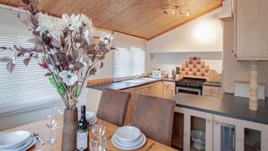 A dining area with a wooden table set for two, a vase of flowers, and a bottle of wine. - A lodge that sleeps 4 guests  in 2 bedrooms (Windermere)