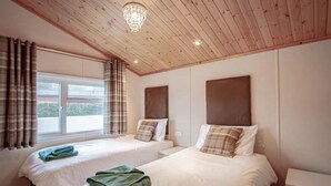 A room with two beds, a chandelier, and a window with curtains. - A lodge that sleeps 4 guests  in 2 bedrooms (Windermere)