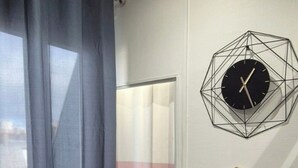 A modern room with a geometric wall clock, a small table with a bottle and glass, and a window with curtains. - Pretty Parisian studio (Paris)