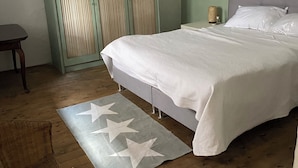 A bedroom with a bed, a nightstand, a wicker chair, a wardrobe, and a hanging light fixture.