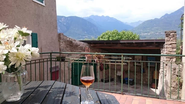 A balcony with a table, a glass of red wine, and a vase of white flowers.
