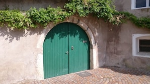 A green double door with a metal handle, set in a stone archway, with a brick-paved area in front.