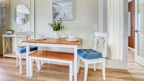 Un comedor con una mesa de madera, sillas blancas y un banco. Hay una planta en maceta sobre la mesa.