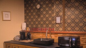 Eine kompakte Küche mit Spüle, Kaffeemaschine, Mikrowelle und einer Uhr an der Wand.