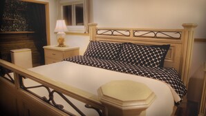 Ein Schlafzimmer mit einem hölzernen Bettgestell, einem Nachttisch mit Lampe und einem Fenster mit Vorhängen.