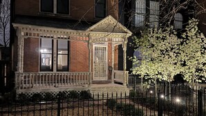 A two-story brick house with a front porch, a visible garage door, and a tree with white blossoms. - Remodeled Old-World Home, Walkable to Rino, Ballpark,& Downtown (Denver)