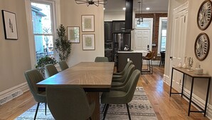 A spacious dining area with a large wooden table, multiple chairs, and a patterned rug. - Remodeled Old-World Home, Walkable to Rino, Ballpark,& Downtown (Denver)