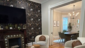 A modern living room with a fireplace, two armchairs, a round coffee table, and a television. - Remodeled Old-World Home, Walkable to Rino, Ballpark,& Downtown (Denver)