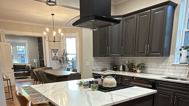 A modern kitchen with a central island, dark cabinetry, and a pendant light. - Remodeled Old-World Home, Walkable to Rino, Ballpark,& Downtown (Denver)