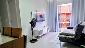A modern living room with a sofa, a TV, a fan, and a dining area with chairs.