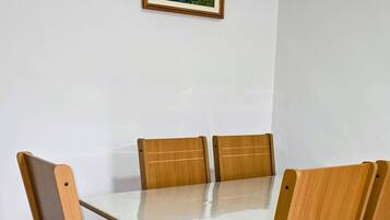 A dining table with four wooden chairs, a framed picture on the wall, and a tiled floor.
