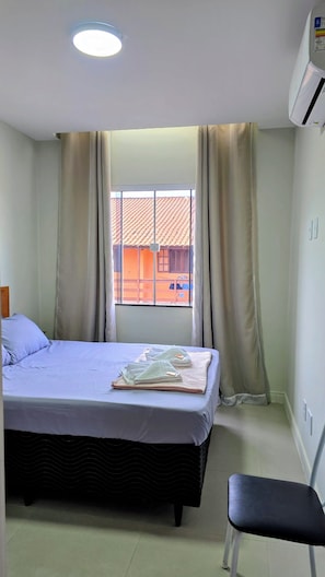 Une chambre d’hôtel avec un lit, une fenêtre avec des rideaux, une chaise et un appareil de climatisation.