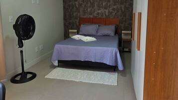 A bedroom with a bed, a standing fan, a wall-mounted air conditioner, and a wooden wardrobe.