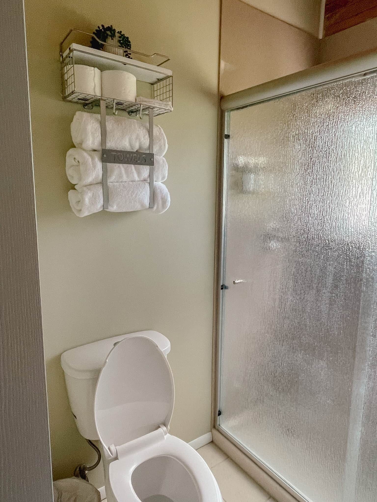 Une salle de bain comprenant des toilettes, un porte-serviettes avec des serviettes et une douche dotée de portes en verre dépoli.