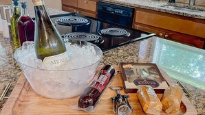Un plan de travail de cuisine avec un saladier rempli de glaçons, une bouteille de vin, un pot de confiture, un ensemble de couteaux et une miche de pain.