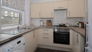 A modern kitchen with beige cabinets, a built-in oven, a dishwasher, and a window with a floral curtain. - in Bournemouth With 2 Bedrooms and 1 Bathrooms (Bournemouth)
