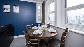 A dining area with a round table set for four, surrounded by wooden chairs, against a blue wall with two framed pictures. - in Bournemouth With 2 Bedrooms and 1 Bathrooms (Bournemouth)