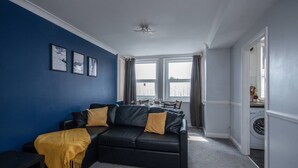 A living room with a black leather sofa, a yellow throw blanket, and three framed pictures on the wall. - in Bournemouth With 2 Bedrooms and 1 Bathrooms (Bournemouth)