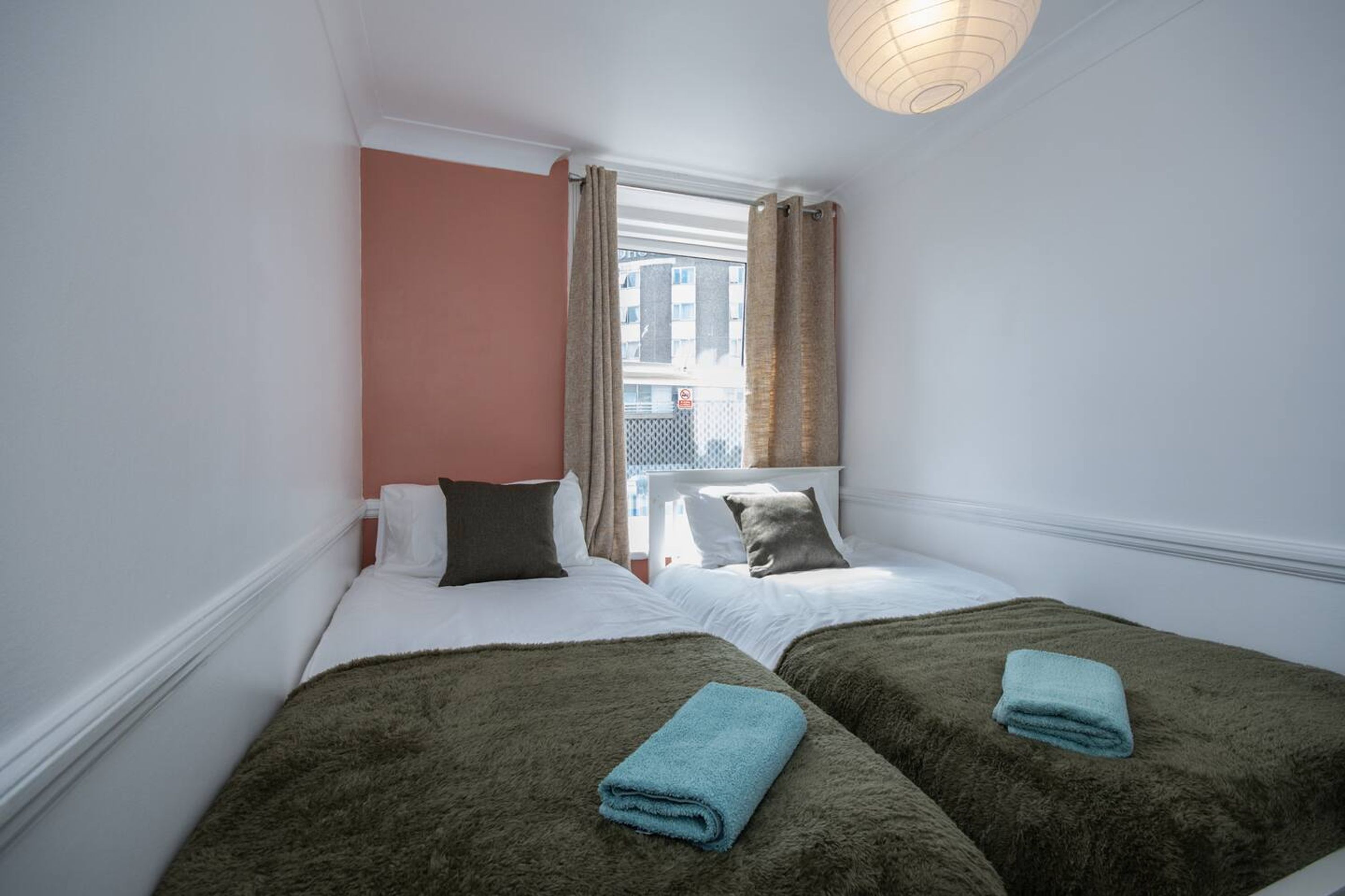 A room with two beds, a window with curtains, and a hanging light fixture.