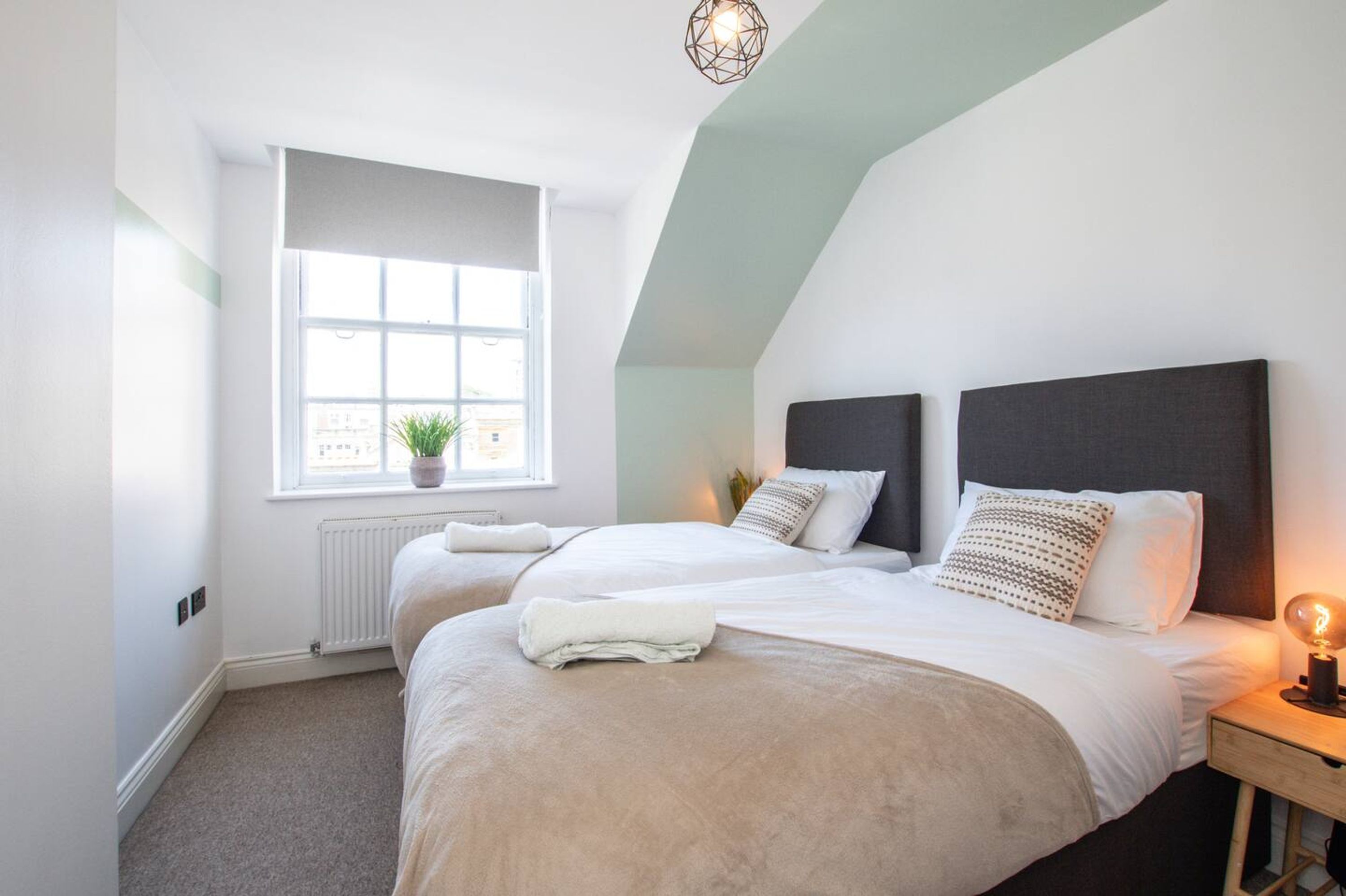 Une chambre avec deux lits, une fenêtre donnant sur un beau paysage, un radiateur et une table de chevet avec une lampe.