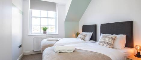 Une chambre avec deux lits, une fenêtre donnant sur un beau paysage, un radiateur et une table de chevet avec une lampe.