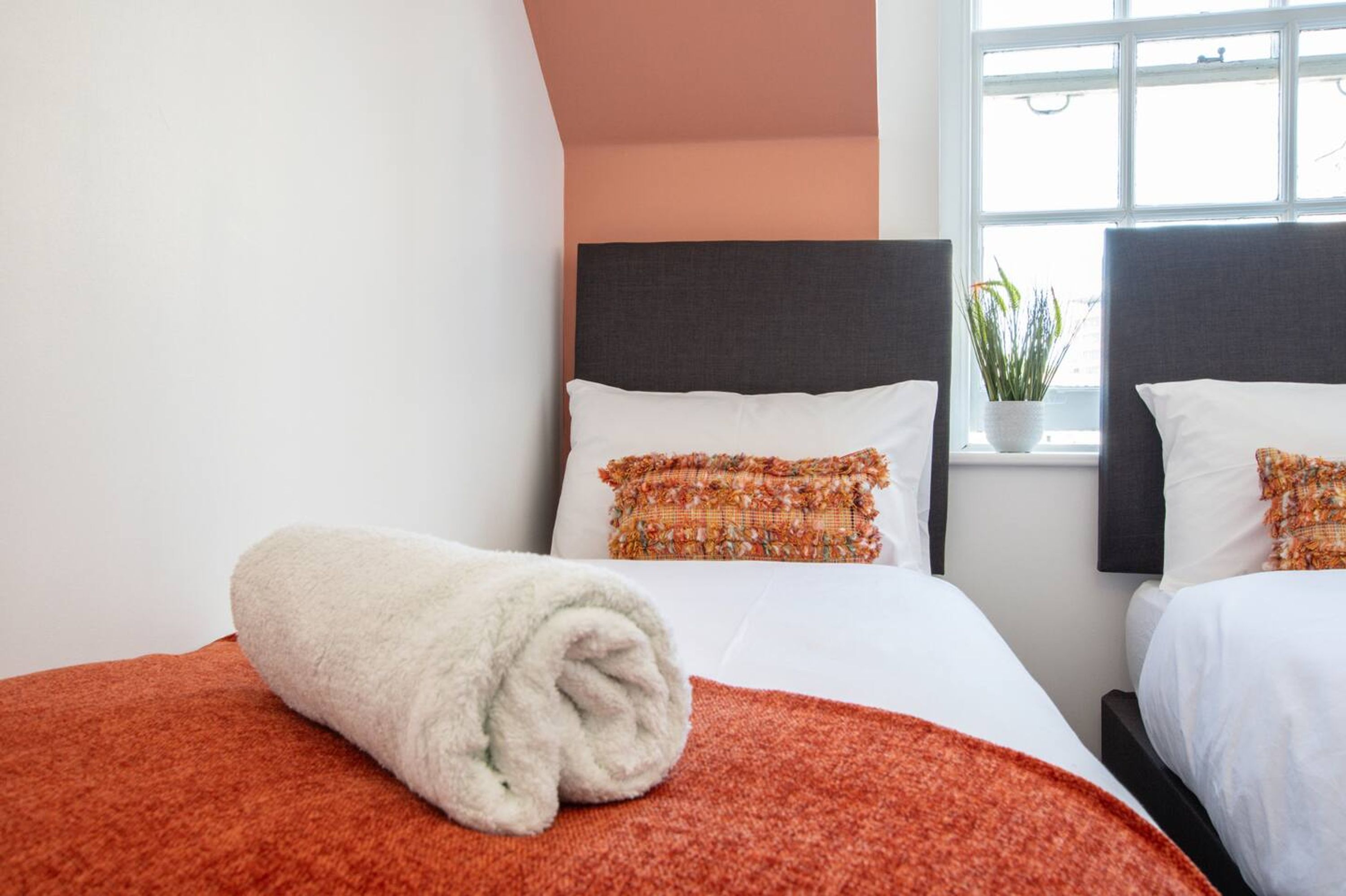 Une chambre d’hôtel avec deux lits, chacun doté d’une tête de lit sombre, de draps blancs et d’une serviette blanche roulée posée sur le lit.