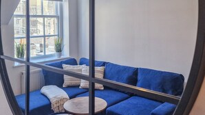 A modern interior with a blue sofa, two small round tables, and a window with a view of buildings. - in Bournemouth With 2 Bedrooms and 1 Bathrooms (Bournemouth)